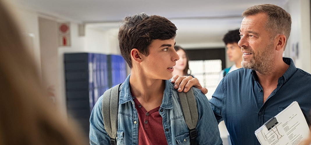 A teacher with a reassuring hand on a student's shoulder, having a supportive conversation in a school hallway,